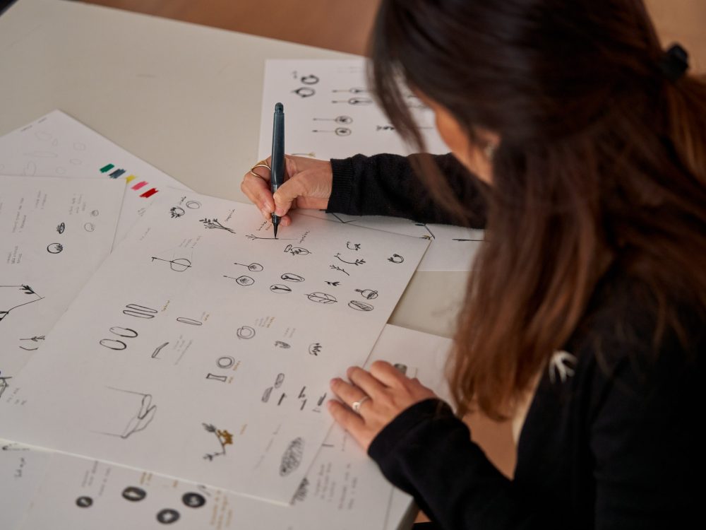 High angle of crop anonymous female designer drawing sketches for handmade accessories on paper in workshop